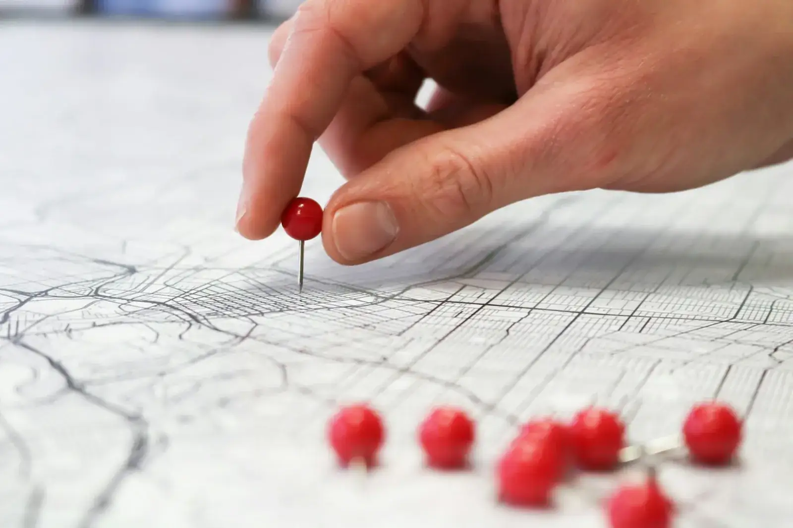 Main posant une épingle rouge sur un plan de ville, avec d’autres épingles au premier plan