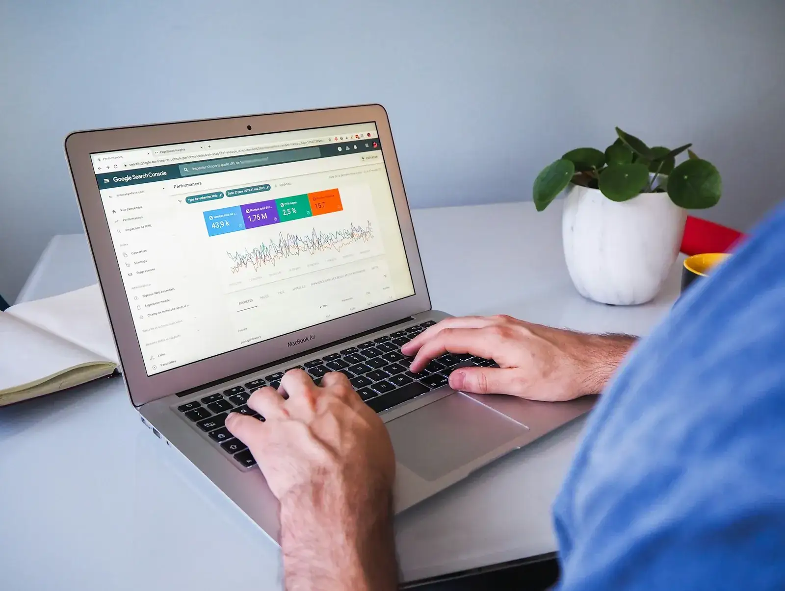 Mains sur un ordinateur portable affichant des statistiques de recherche, près d’une plante
