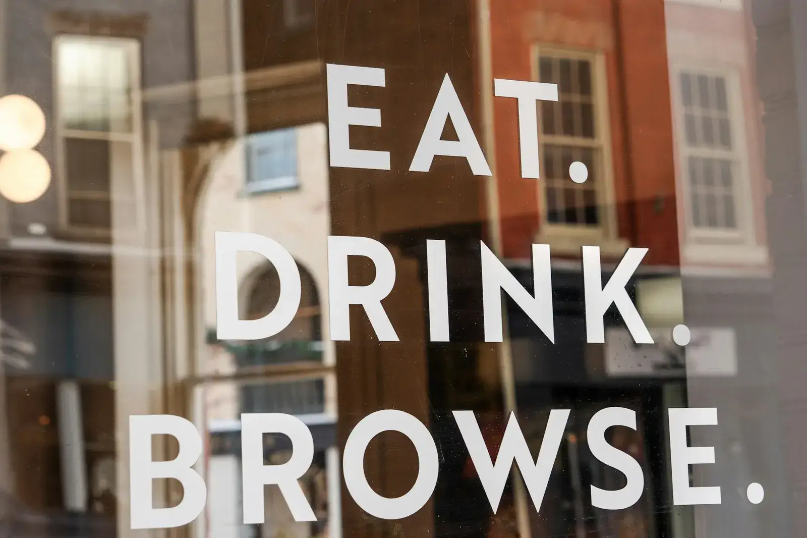 Lettrage blanc « Eat. Drink. Browse. » posé sur la vitre d’un commerce