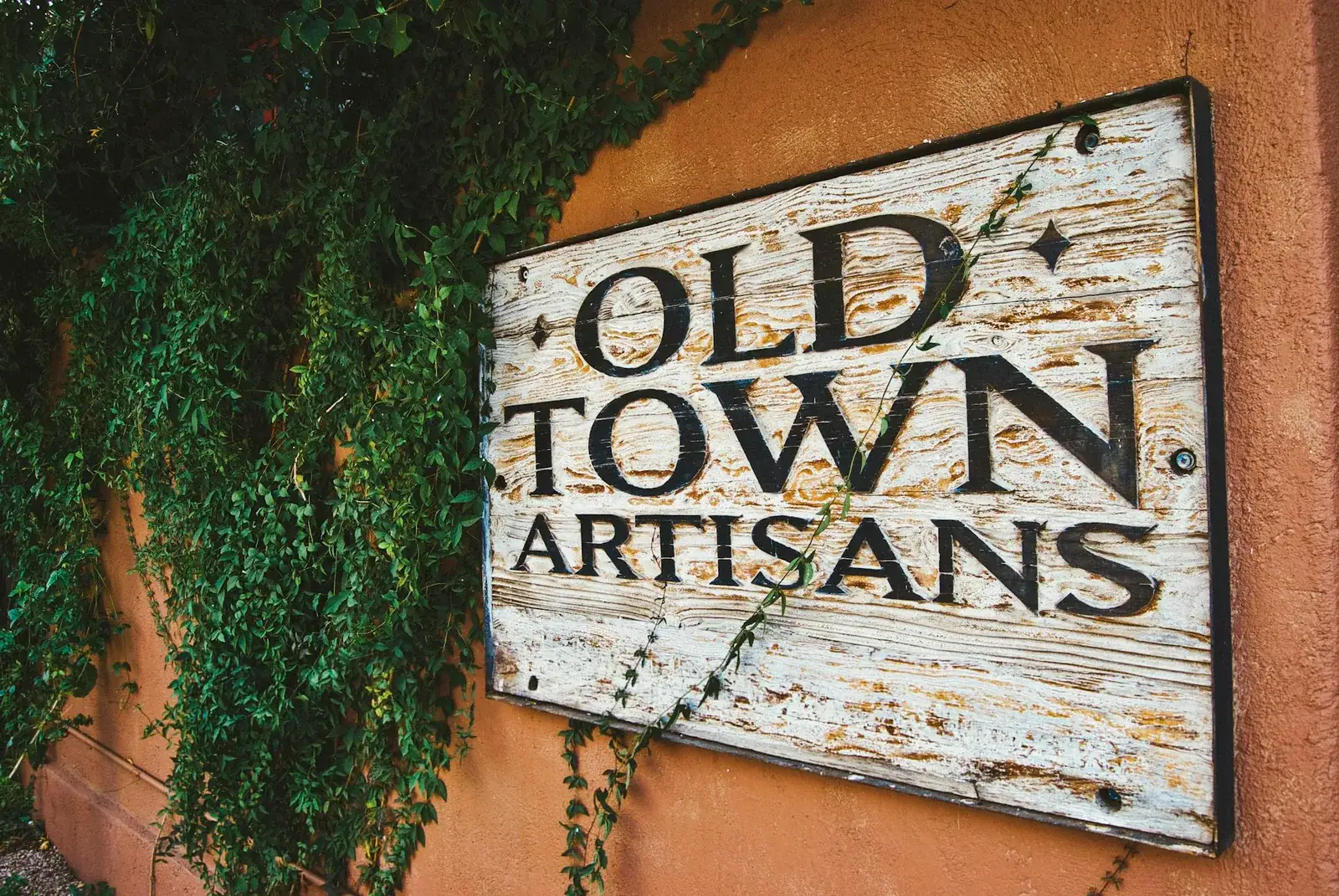 Enseigne en bois patiné « Old Town Artisans » fixée sur une façade ornée de lierre