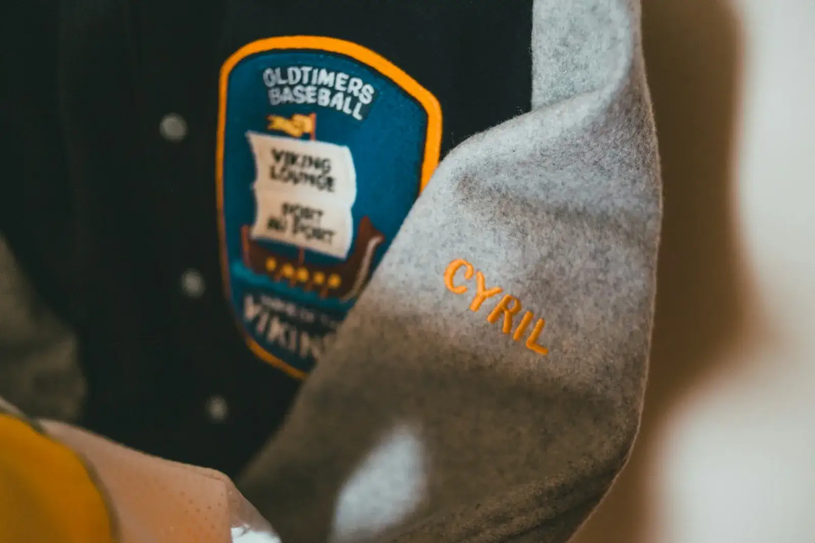 Manche d’une veste portant un écusson brodé et un prénom brodé en fil orange