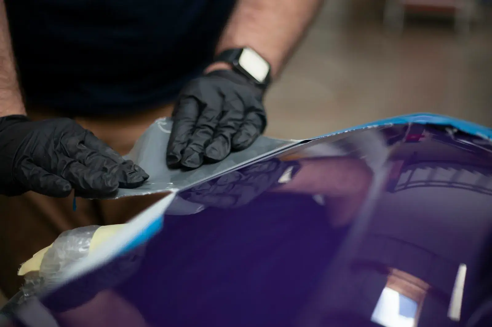 Pose d’un film adhésif sur la carrosserie d’un véhicule, par des mains gantées