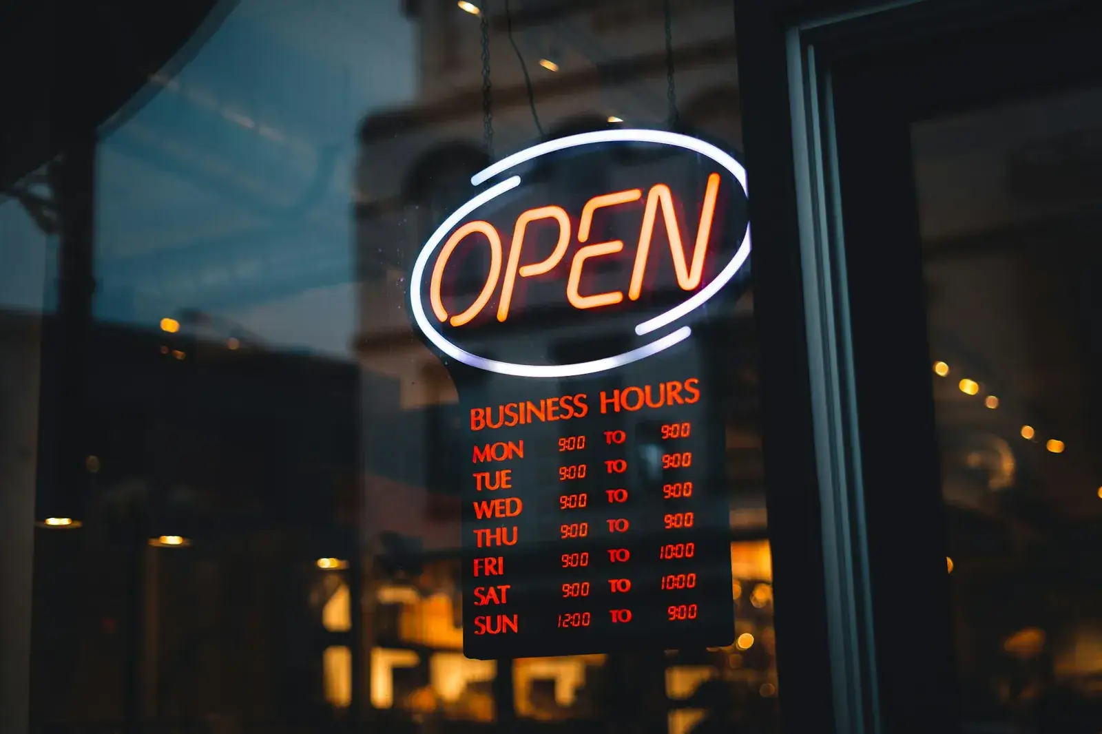 Enseigne lumineuse « Open » et tableau des horaires d’ouverture, dans une vitrine de nuit